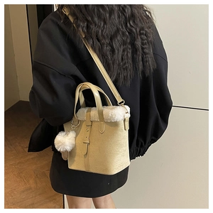 Detail of beige bucket bag featuring white faux fur trim and soft plush ball pendant