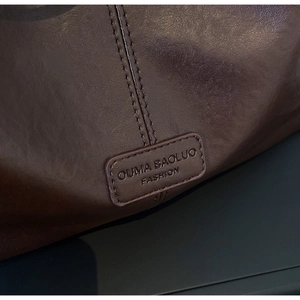Détail du sac cabas en cuir marron foncé avec étiquette cousue et texture brillante