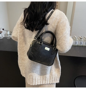 Detail view of a black Boston bag with a gold metal plate and pebble grain leather texture