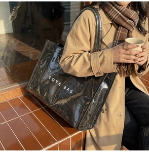 Close-up of a large black glossy tote bag with white TOTE BAG text in a street setting