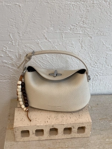 Chic beige pebbled leather handbag with silver twist lock and wooden bead charm on stone