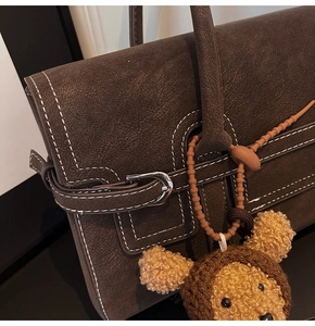 Detailed close-up of retro brown leather handbag with contrast stitching and bear charm