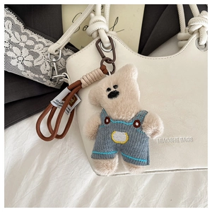 Close-up of cute bear plush charm with blue knit overalls on a white leather bag