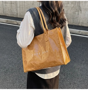 Detail of a large translucent ginger brown PVC tote bag held by a model on a street