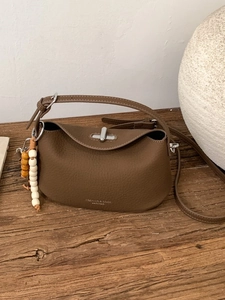 Brown litchi leather crossbody bag with wooden bead charm on a rustic wooden desk