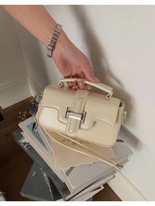 Detail of cream crossbody square bag with silver clasp against a vintage book background