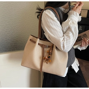 Detail of beige suede tote bag with brown leather handles and ethnic bead pendant