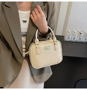Detail of a minimalist cream bowling handbag with gold metal hardware and smooth PU texture