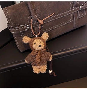 Close-up of a teddy bear plush charm with a brown knit hoodie on a leather handbag