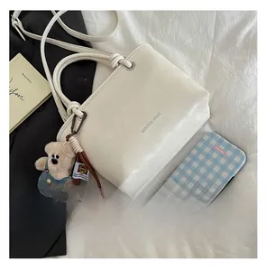 Detail of cream white leather bucket bag with brand logo and cute bear plush charm