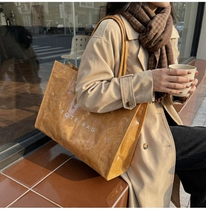 Detail of a brown tote bag with pleated texture and TOTE BAG print worn outdoors