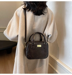 Dark brown retro Boston bag shown on a model wearing a beige coat in a modern setting
