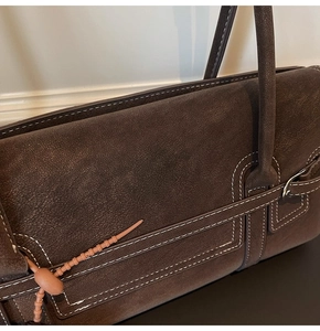 Detail of dark brown leather tote bag with white contrast stitching and metal hardware