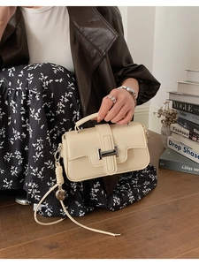 Detail of cream leather crossbody bag with silver square buckle and heart charm strap