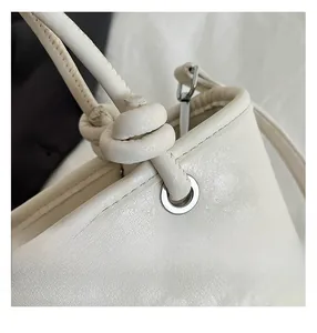 Detail of knotted shoulder strap and silver eyelet on a beige leather shoulder bag