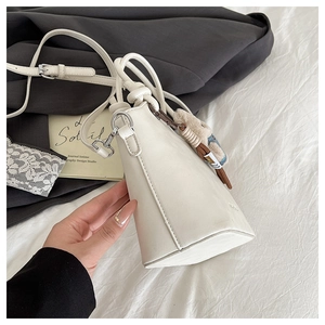 Detailed view of white bucket bag with drawstring knot and brown teddy bear charm