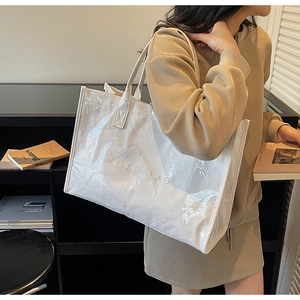 Close-up of a white glossy tote bag with embossed TOTE BAG lettering worn on shoulder