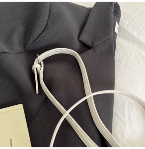 Close-up of off-white leather shoulder strap with silver buckle on gray blazer