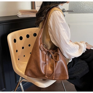 Détail d'un sac hobo en cuir marron avec un nœud décoratif et un logo discret embossé