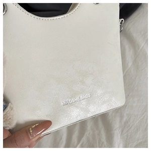Detail of white bucket bag featuring silver MIAOSHE BAGS logo and plush charm