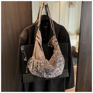Detail of sequined handbag with brown suede top and decorative drawstring hanging on a hook