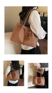 Detail of brown tote bag featuring matte leather texture and wooden bead tassel accessory