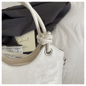 Close-up of cream leather bucket bag showing knotted strap and silver eyelet detail