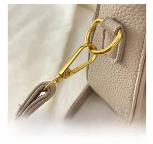 Détails macro de la quincaillerie dorée et du cuir à motif litchi de ce sac à bandoulière