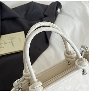 Close-up of cream white bucket bag featuring knotted handle and silver metal zipper detail