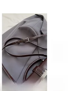 Detail of a dark brown shoulder strap with a silver square metal buckle on a grey blazer