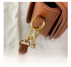 Vue macro détaillée du fermoir mousqueton en métal doré sur un sac en cuir marron
