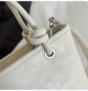 Detail of a white bucket bag featuring leather texture, knot strap, and metal eyelets
