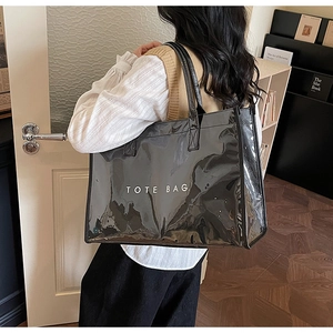 Detail of glossy black tote bag with white TOTE BAG text shown in a cozy indoor setting