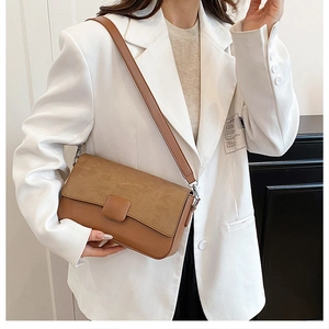 Close-up of brown textured leather shoulder bag worn by model in white blazer