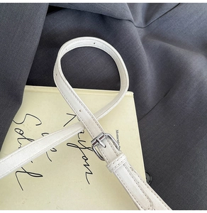Close-up of a slim white leather belt with a silver square buckle on a grey suit