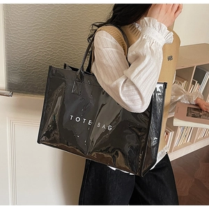 Close-up of glossy black tote bag with white TOTE BAG text in home setting