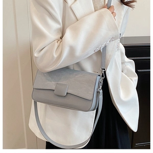 Close-up of light blue textured leather crossbody bag with square buckle detail on white suit