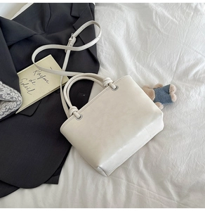 Close-up of cream leather bucket bag with knot handle and metal eyelets on white bedding