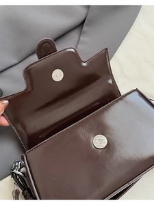 Detail of dark brown leather handbag showing silver magnetic closure and stitching