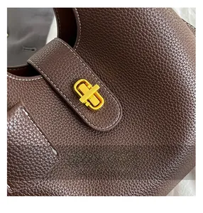 Macro detail of dark brown litchi grain leather bag with white contrast stitching and gold lock