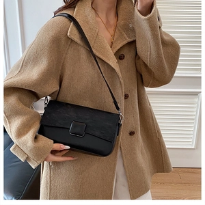 Detail of black leather crossbody bag with textured flap on a beige wool coat