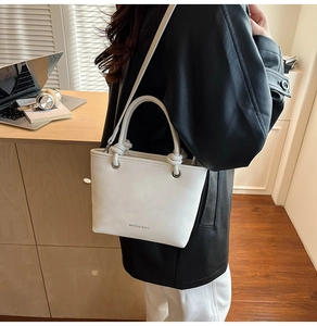 Close-up of stylish white leather bucket bag with knotted handles and thin strap