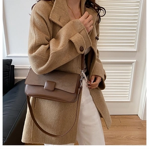 Detail of dark brown leather crossbody bag with wood grain texture worn over a camel coat