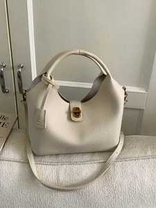 Chic beige lychee leather bucket bag with gold twist lock and shoulder strap on sofa