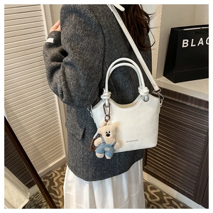 Detailed shot of white faux leather bucket bag with cute bear charm and logo branding