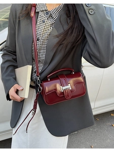 Detail of burgundy crossbody bag with silver H-buckle on grey suit background