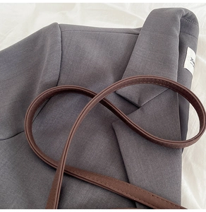 Détail d'une bandoulière en cuir marron foncé avec coutures sur veste grise