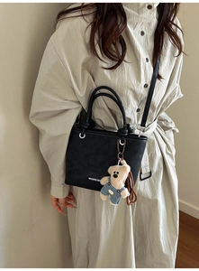 Detail of black leather bucket bag with white typography and cute bear plush charm