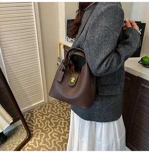 Detail of coffee brown lychee pattern leather bucket bag with golden twist lock on model