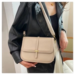 Détail d'un sac bandoulière beige en cuir avec boucles dorées porté par un mannequin